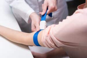 A close up of a doctor tightening the tourniquet on a patient's arm for blood extraction