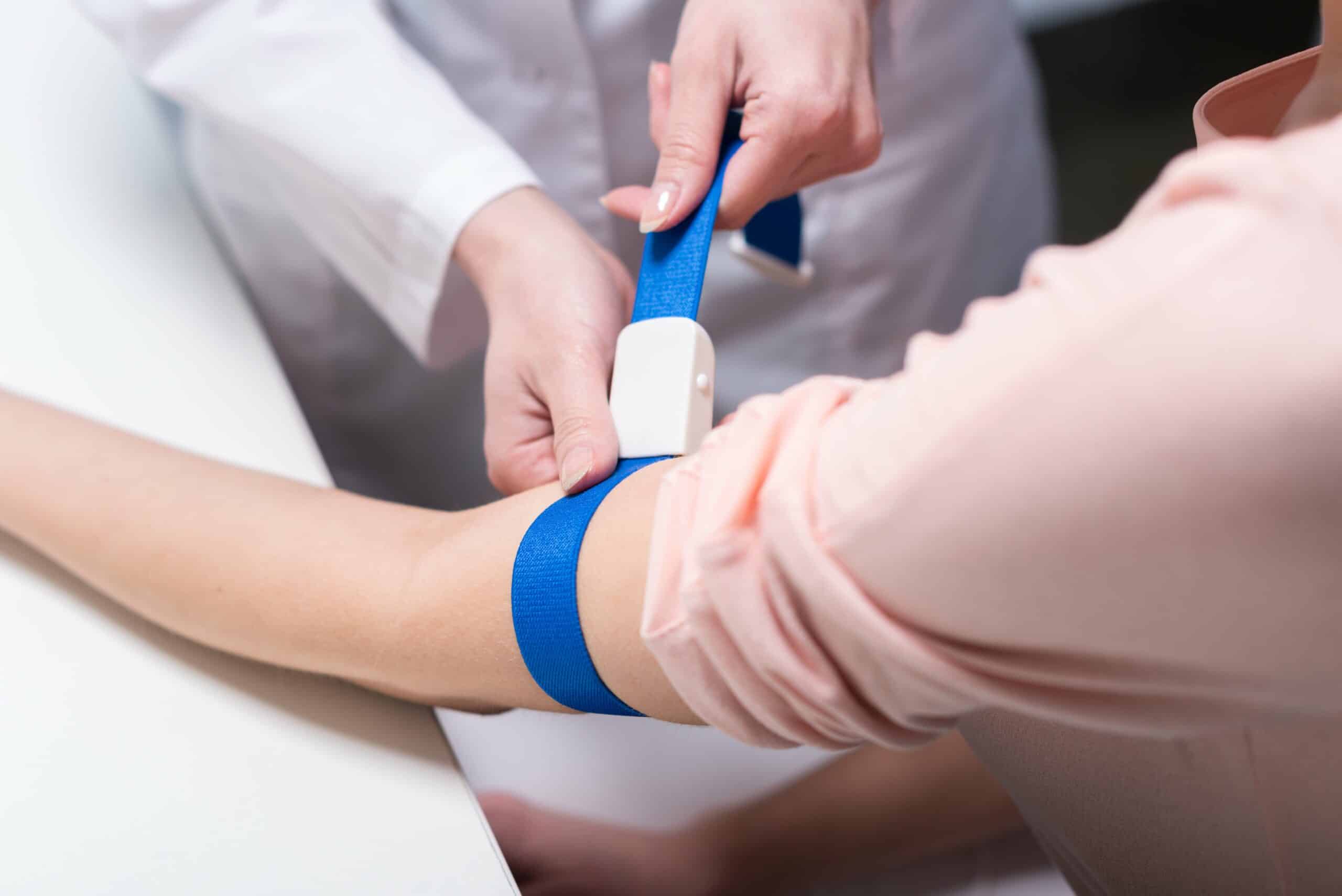 A close up of a doctor tightening the tourniquet on a patient's arm for blood extraction