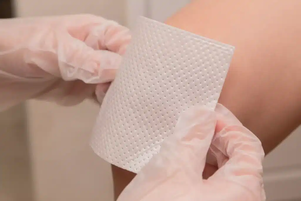 A person wearing latex gloves is placing a bandage on a knee 
 First Aid Pro