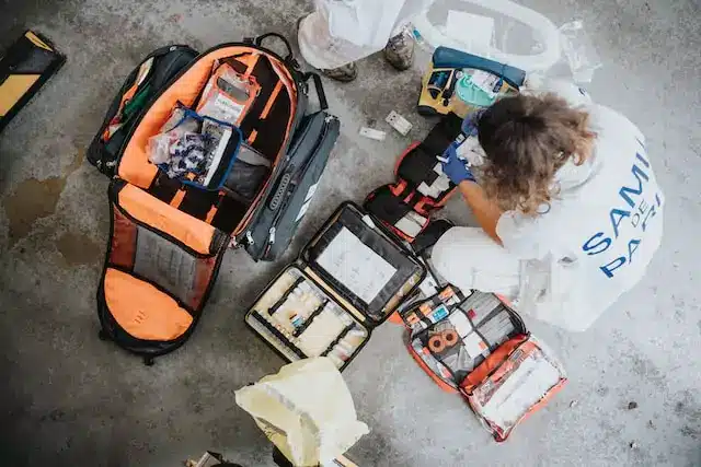 A person sitting on the floor with a backpack and medical supplies, ready to provide aid and assistance.
