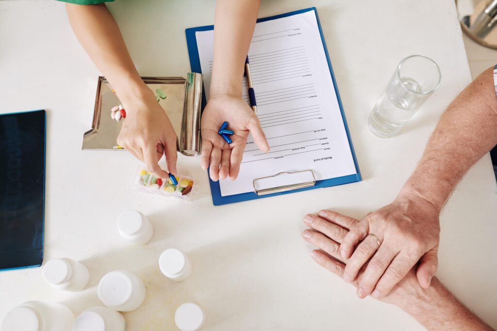 Hands of doctor filling medical card of senior patient and explaining what pills he should take on daily basis, view from above