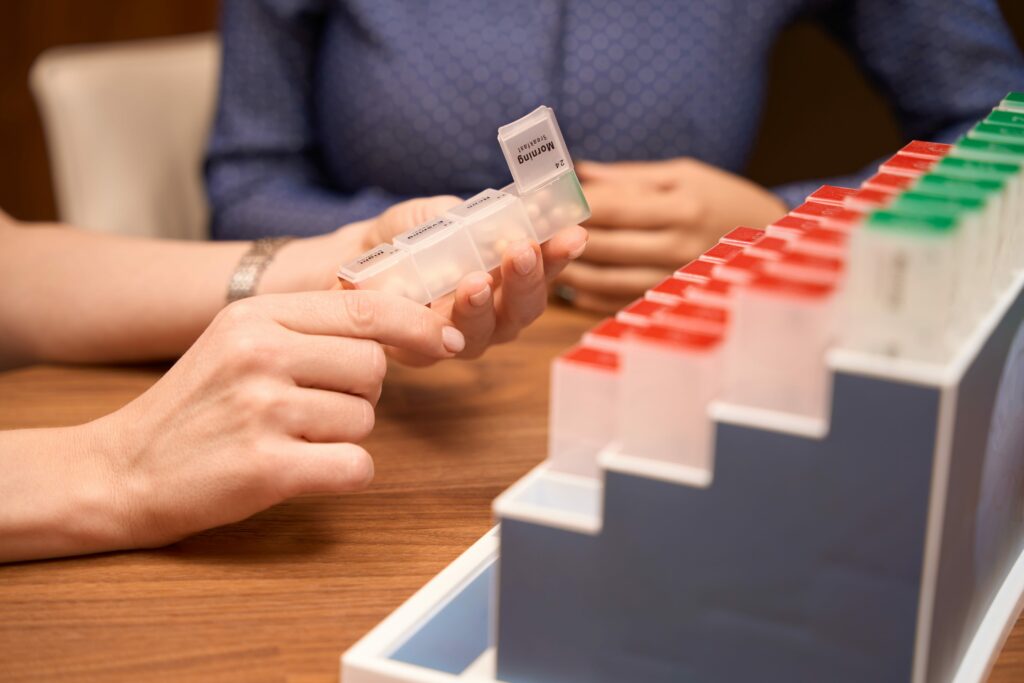 Doctor sitting by the table with patient, holding case for pills and showing it to patient