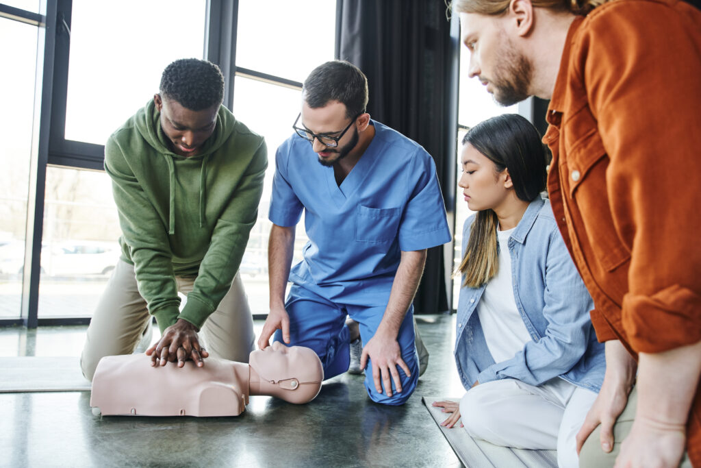 medical instructor looking at man doing chest compressions on CPR manikin, cardiopulmonary resuscitation, first aid training seminar