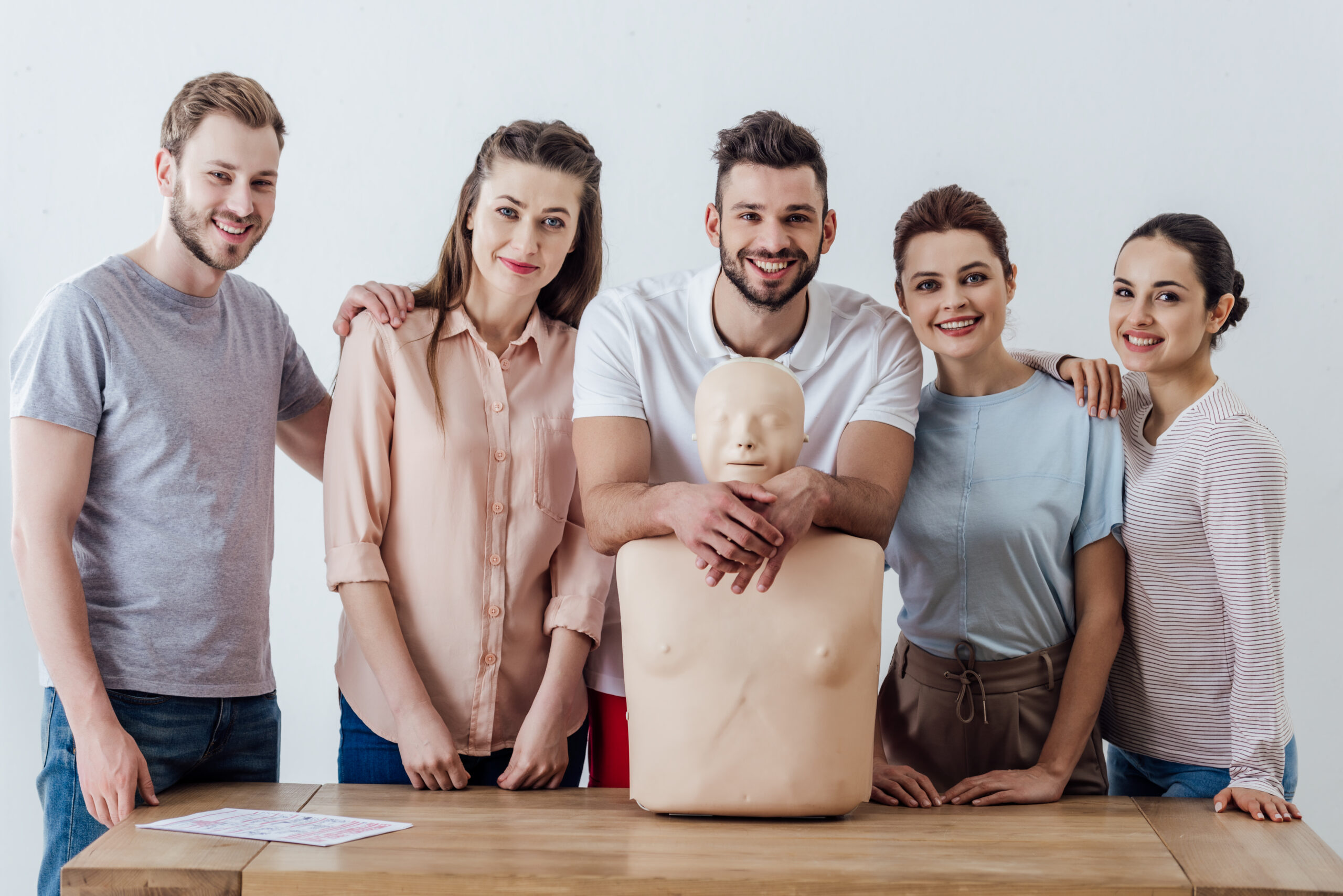 group of people with cpr dummy looking at camera and smiling during first aid training class