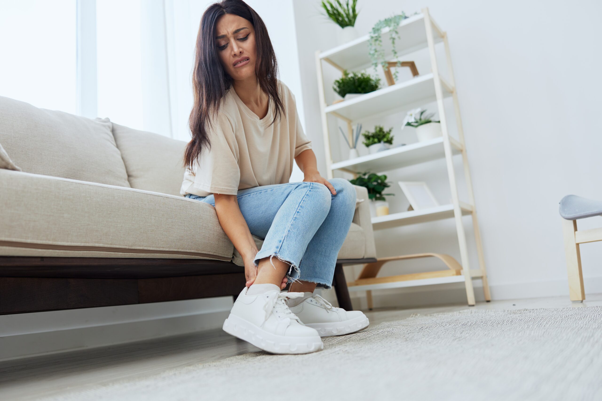 Woman sitting on the couch at home leg and foot pain, sprain and muscle strain, leg injury