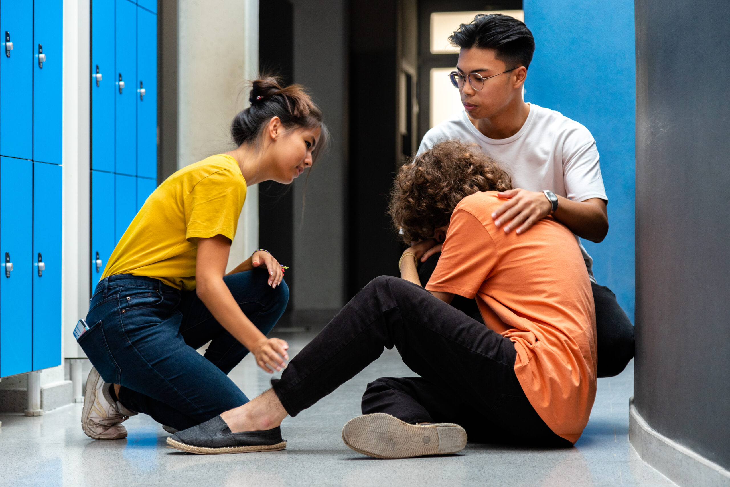Two teen asian high school students comfort sad and depressed classmate victim of bullying in corridor.