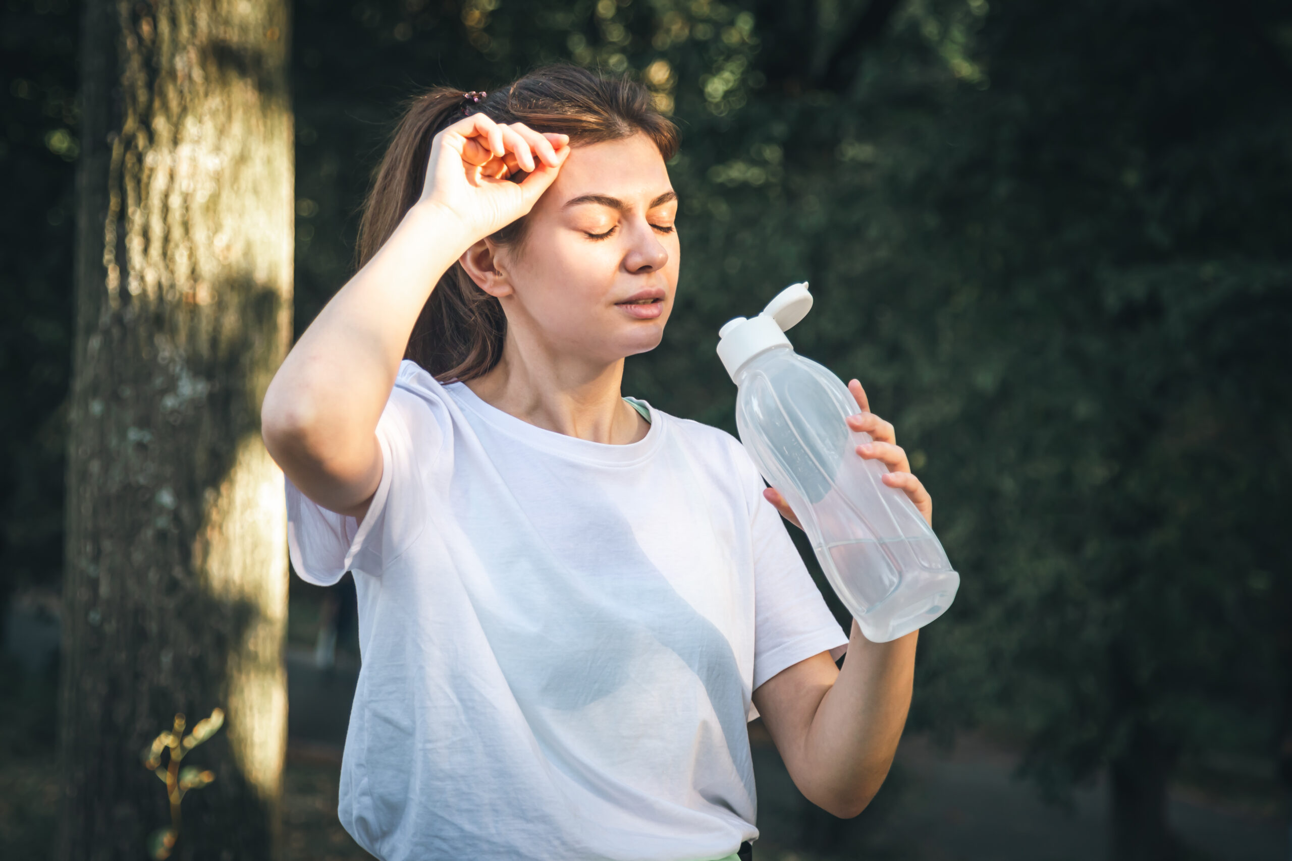 Attractive young woman drinks water after jogging in the park, training in nature.