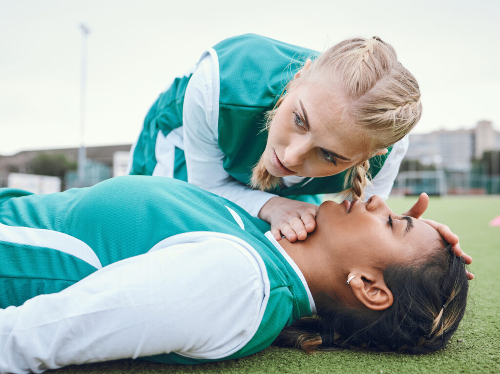First aid, cpr and breathing with a hockey player on a field to save a player on her team after an .