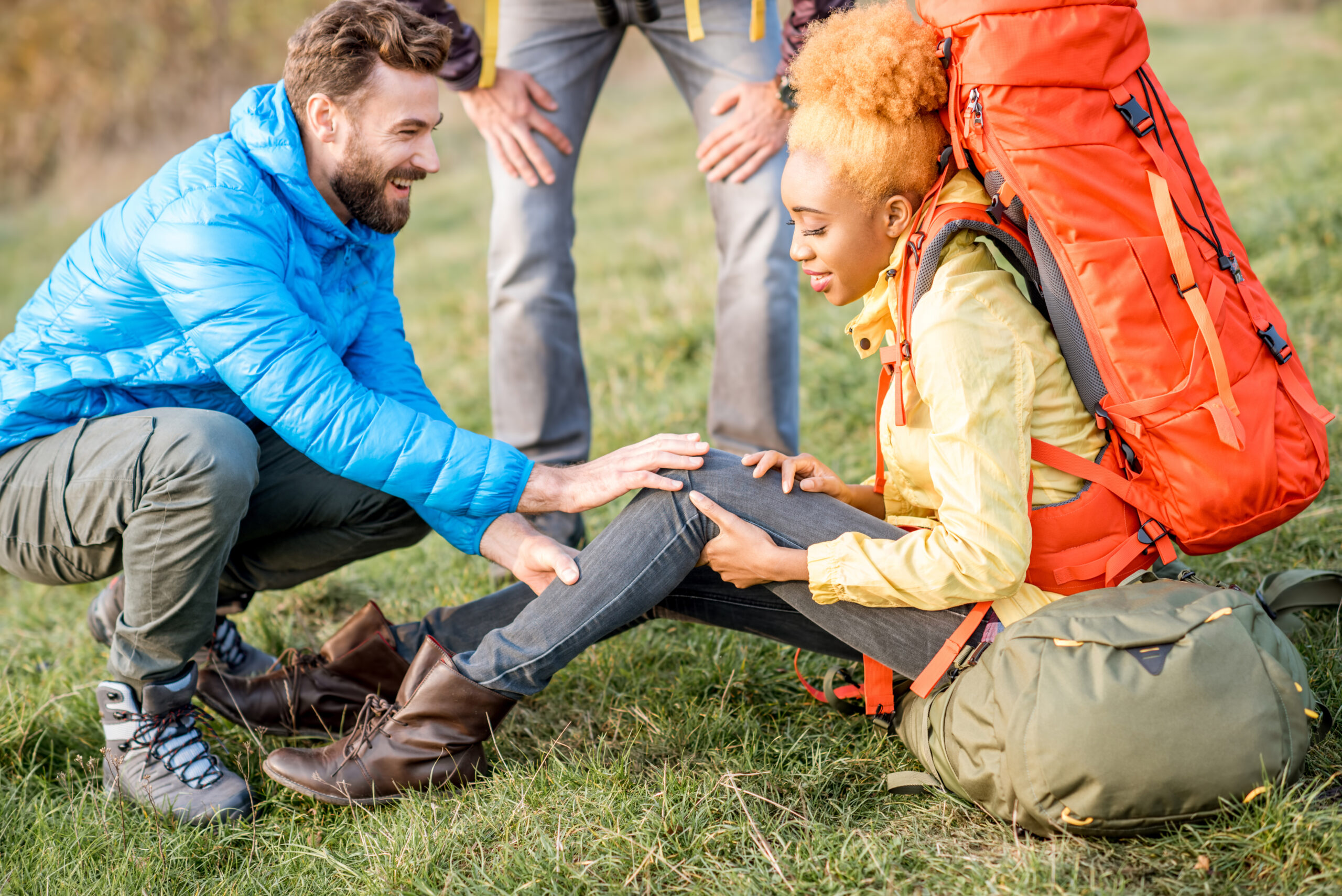 Young african woman with backpack having a trauma with knee hiking with friends outdoors