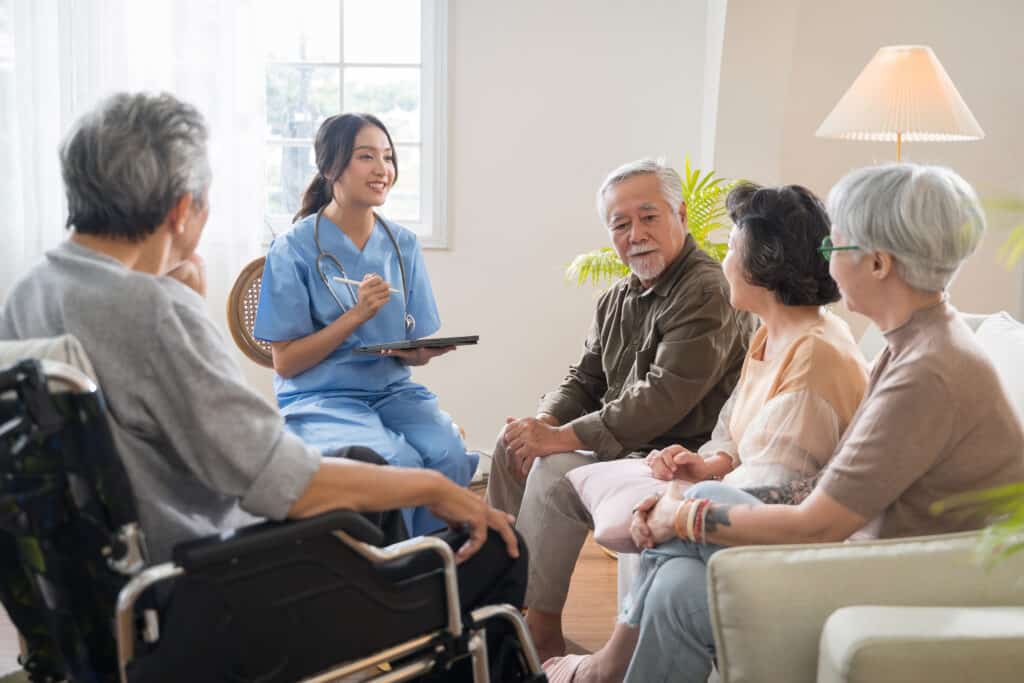 Group of Asian senior people sit in a circle in a nursing home and listen to nurse during a group elderly therapy session.